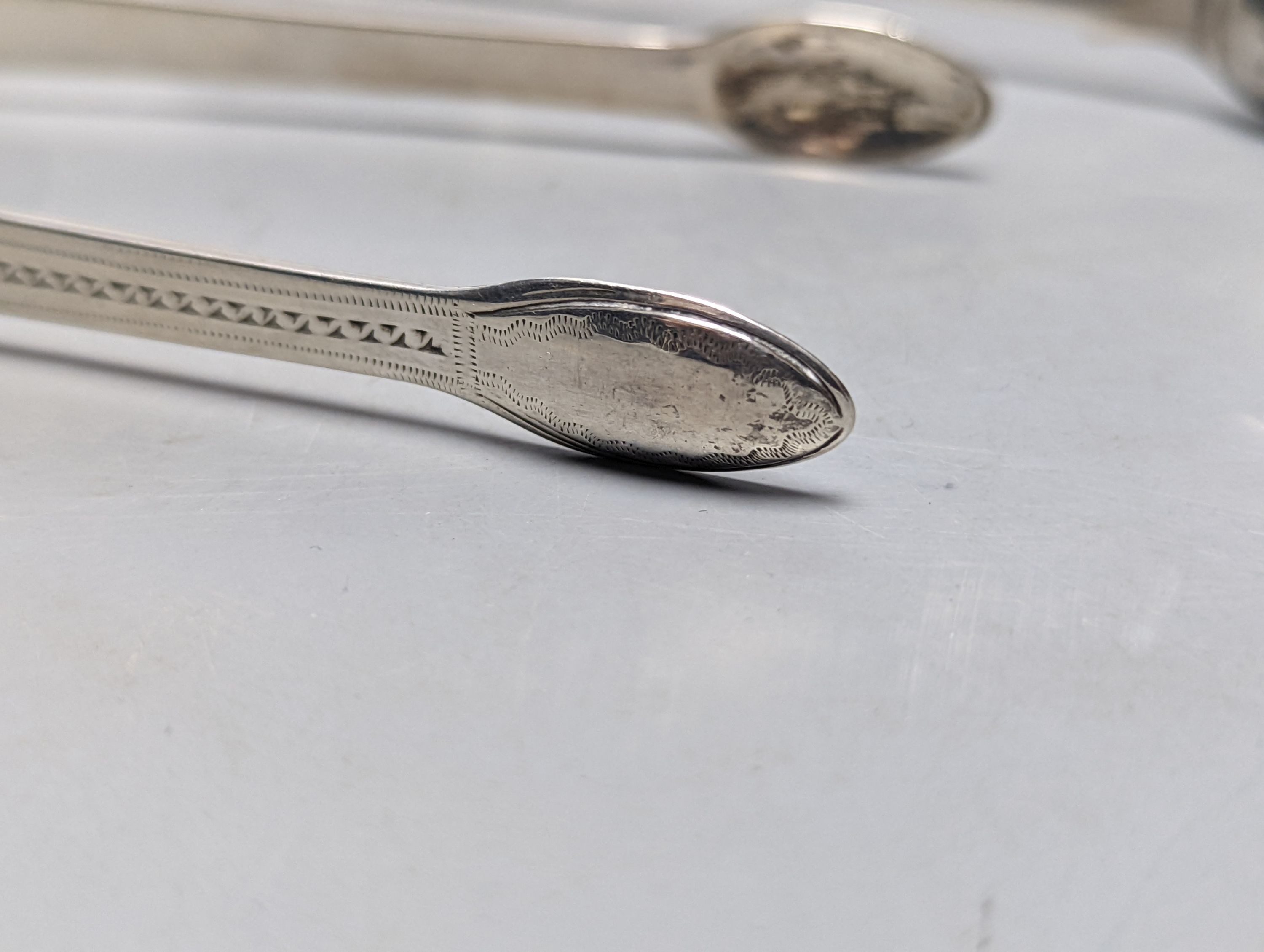 Two pairs of George III bright cut engraved silver sugar tongs and a pair of George IV silver sugar tongs, various dates and makers